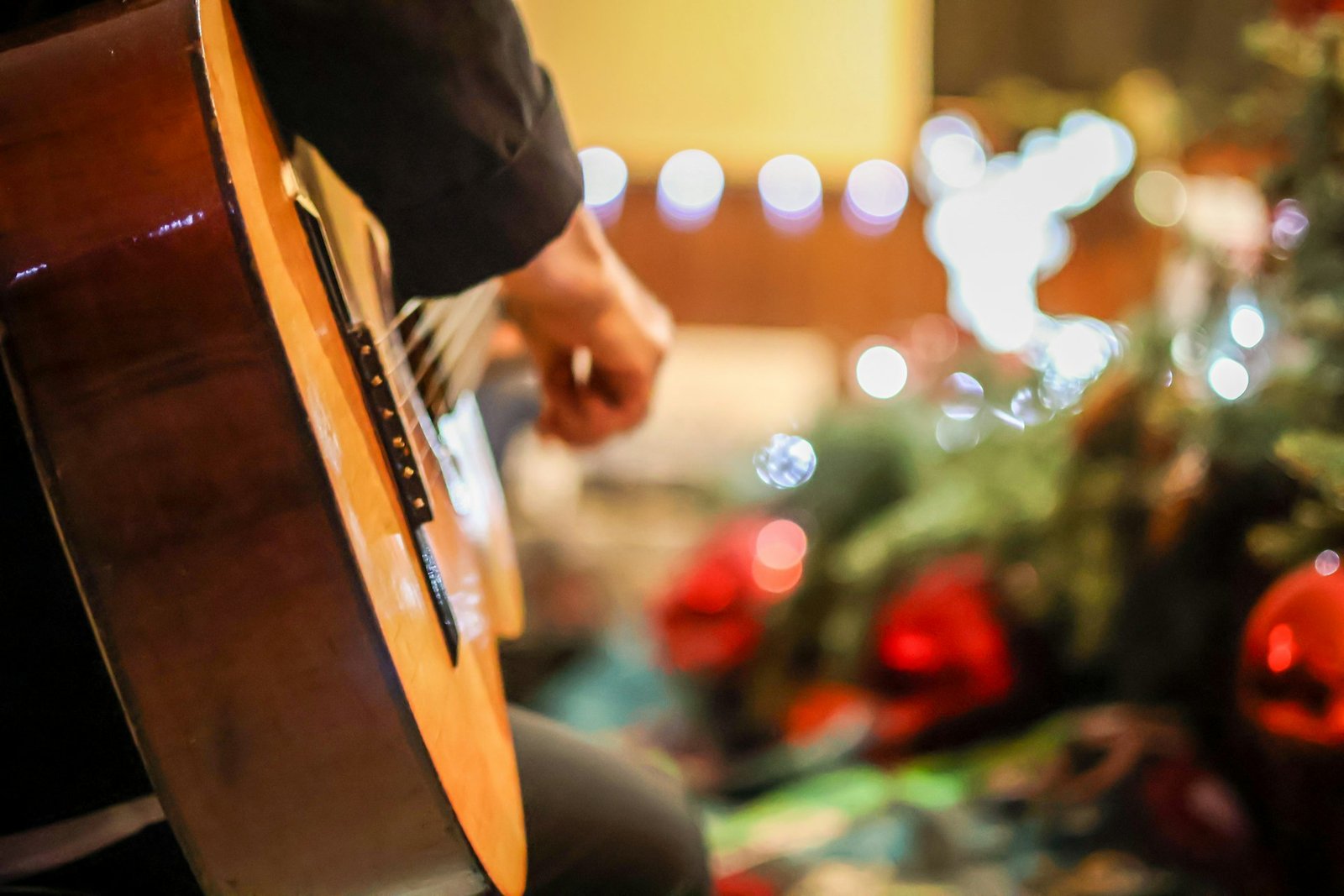 Someone playing an acoustic guitar in front of a Christmas tree
