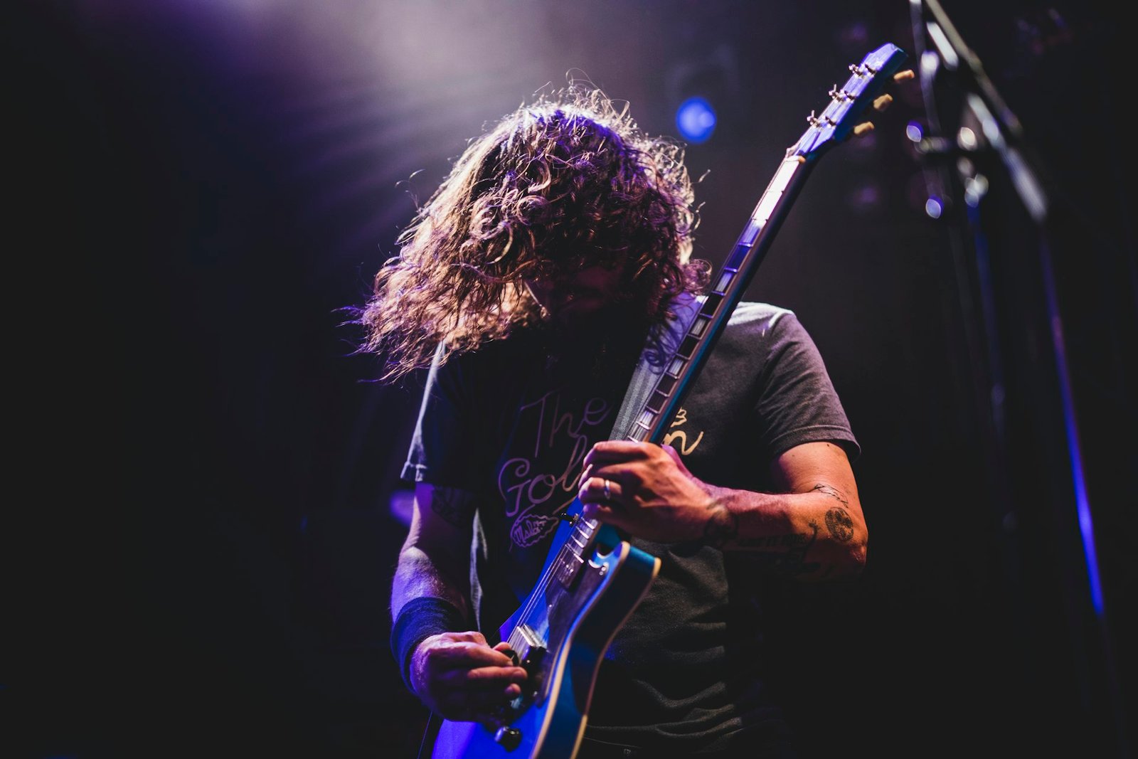 A guitarist playing an electric guitar on stage under blue lights