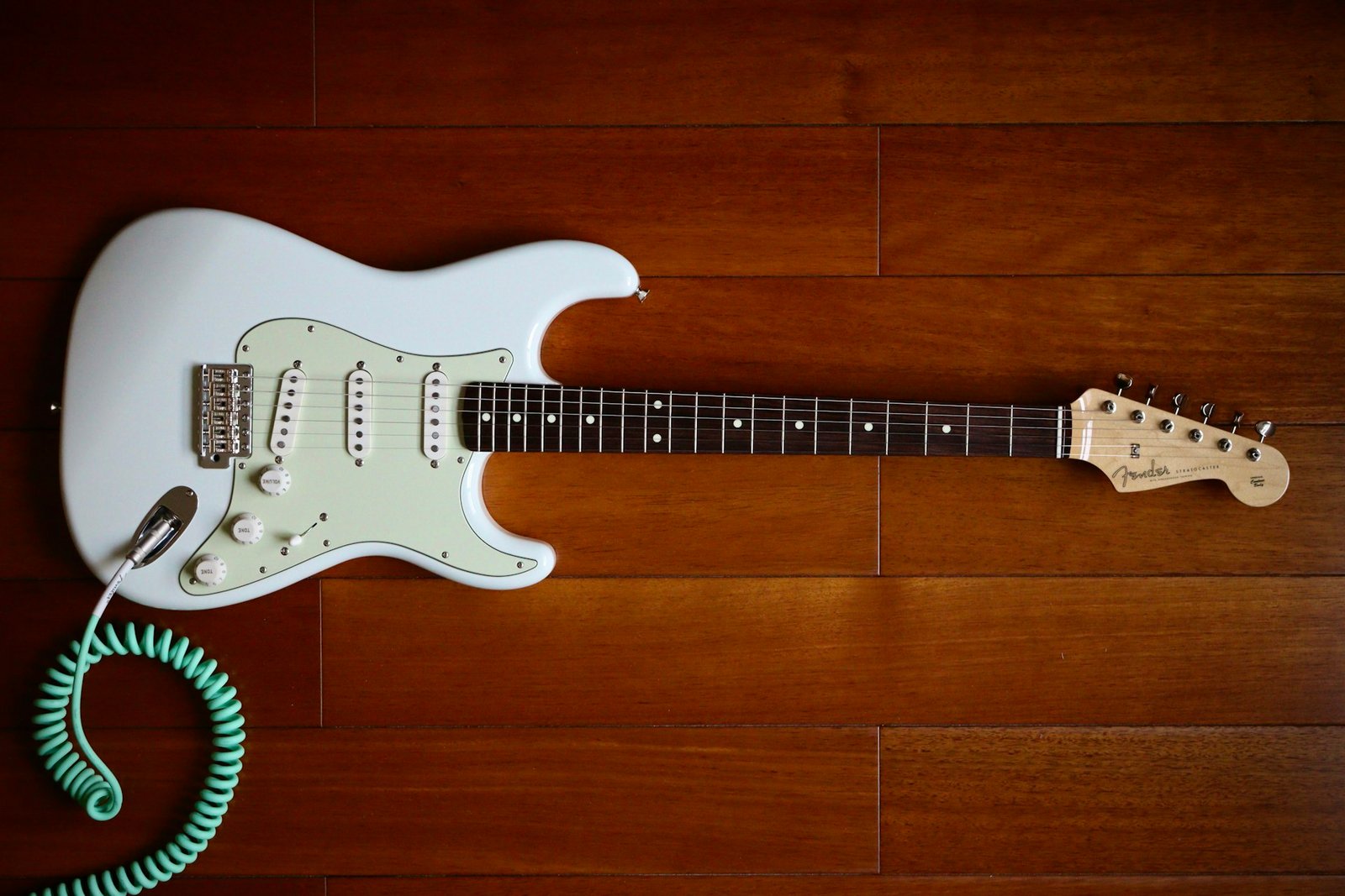 A white S-style electric guitar lying on a wooden floor